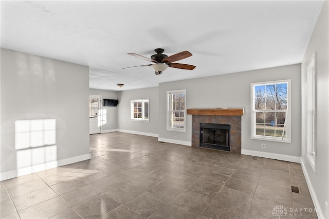 unfurnished living room with a tiled fireplace, plenty of natural light, and baseboards