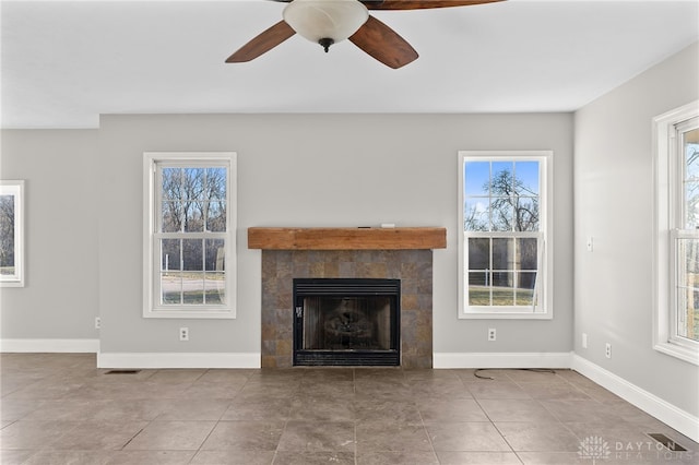 unfurnished living room with a tiled fireplace, baseboards, and a wealth of natural light