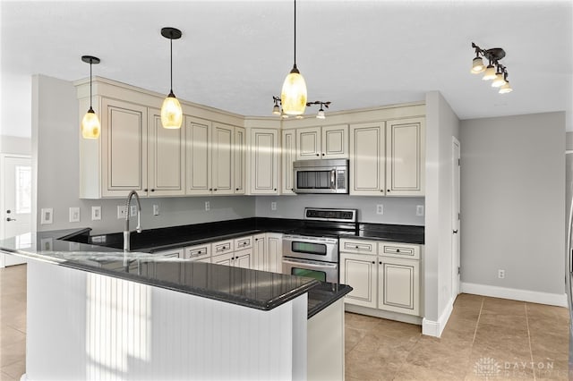 kitchen featuring cream cabinets, a peninsula, a sink, appliances with stainless steel finishes, and decorative light fixtures