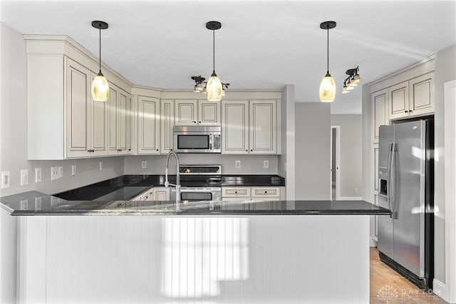 kitchen with a peninsula, appliances with stainless steel finishes, cream cabinetry, dark stone counters, and pendant lighting