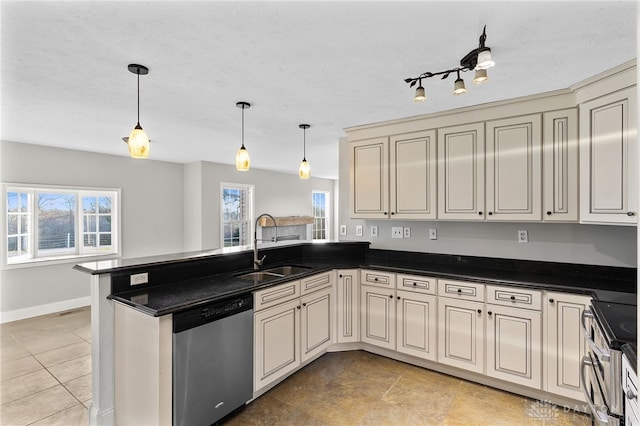 kitchen featuring dark countertops, a peninsula, cream cabinets, stainless steel appliances, and a sink