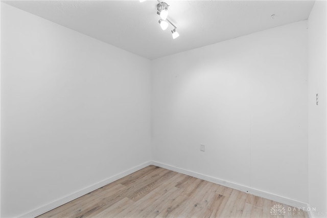 spare room featuring light wood finished floors, baseboards, and rail lighting