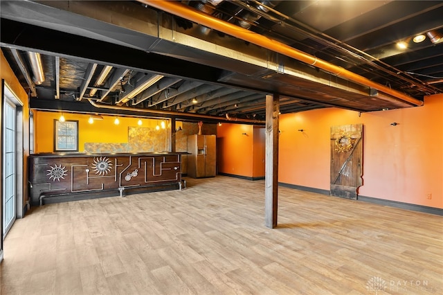 finished below grade area with white refrigerator with ice dispenser, wood finished floors, and baseboards