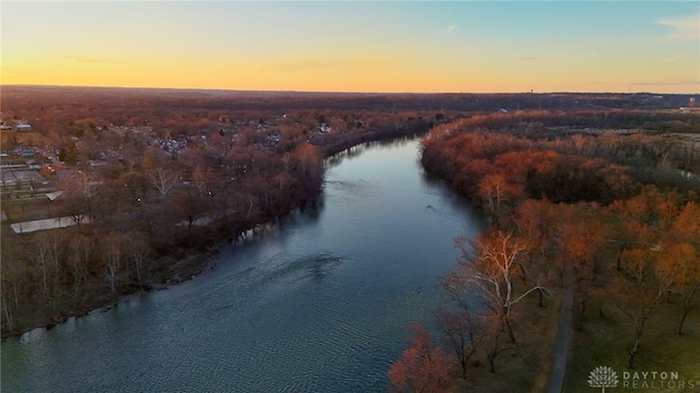 aerial view at dusk featuring a water view and a wooded view