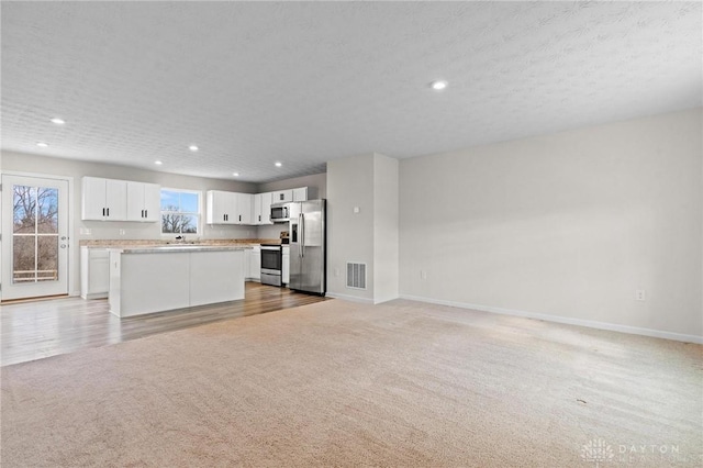 kitchen featuring appliances with stainless steel finishes, visible vents, light carpet, and white cabinetry