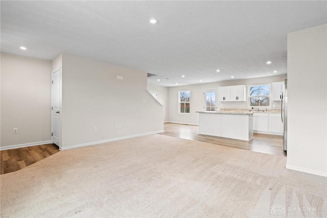 unfurnished living room featuring baseboards, recessed lighting, and light colored carpet