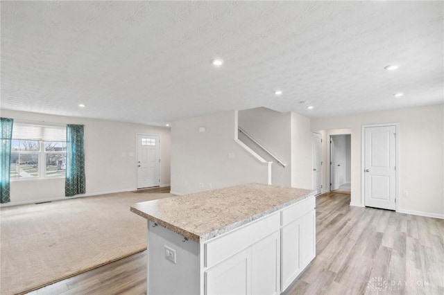 kitchen with light wood finished floors, baseboards, a center island, light countertops, and white cabinetry