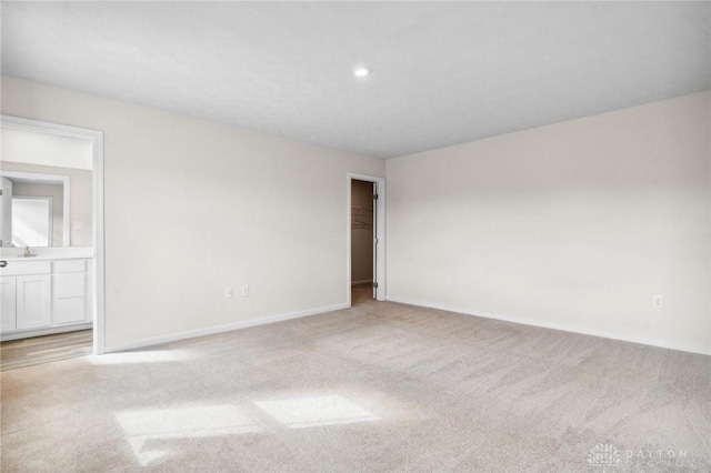 unfurnished room featuring light carpet, baseboards, a sink, and recessed lighting