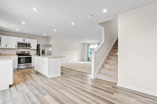 kitchen with appliances with stainless steel finishes, a kitchen island, light wood-style flooring, and white cabinets