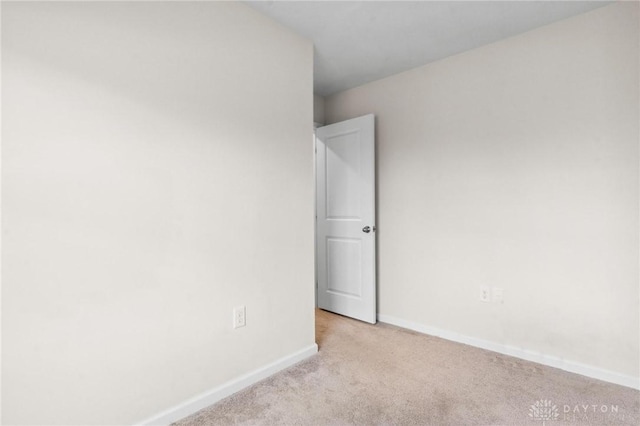 spare room featuring light carpet and baseboards