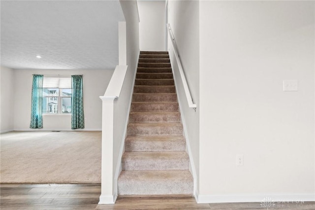 stairs with a textured ceiling, carpet floors, wood finished floors, and baseboards