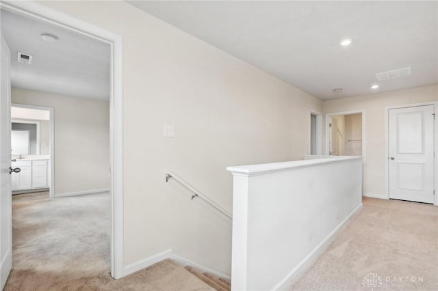 corridor with light carpet, visible vents, baseboards, and an upstairs landing