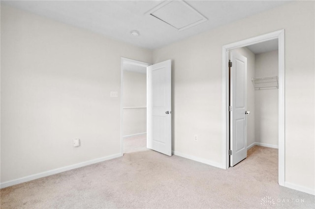 unfurnished bedroom featuring light carpet, a spacious closet, attic access, and baseboards