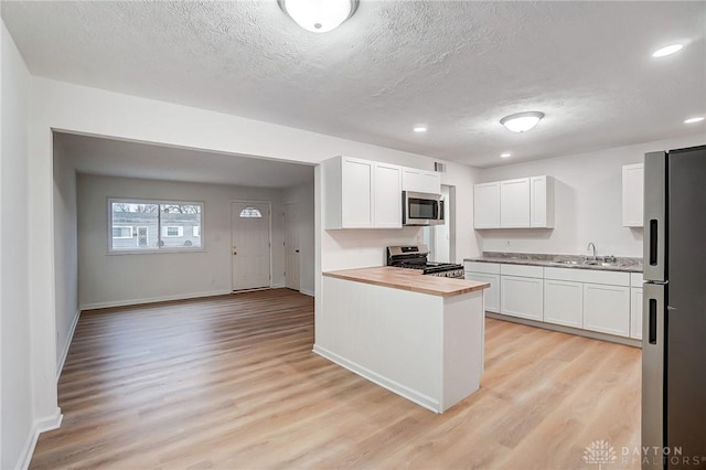 kitchen with stainless steel appliances, butcher block counters, a sink, white cabinets, and light wood finished floors