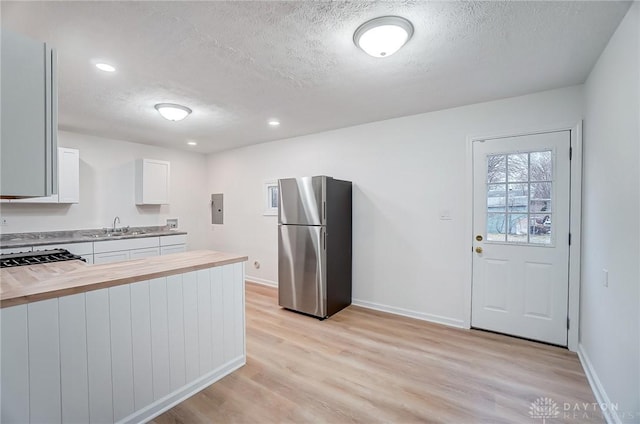 kitchen featuring a sink, wood counters, freestanding refrigerator, and light wood-style floors