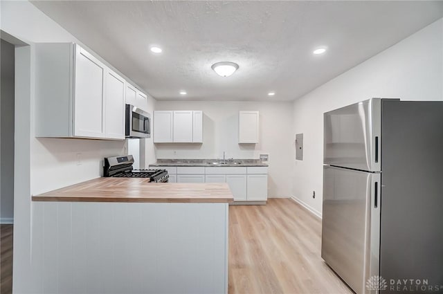 kitchen featuring light wood-style flooring, stainless steel appliances, butcher block counters, a sink, and white cabinetry