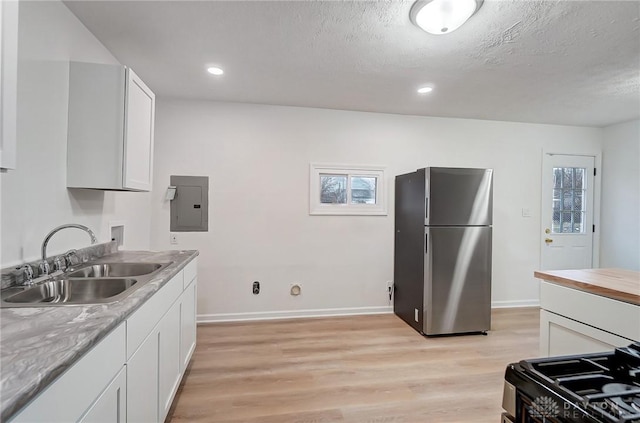 kitchen with light wood-style floors, a sink, freestanding refrigerator, and electric panel