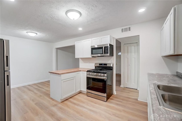 kitchen featuring light wood finished floors, visible vents, butcher block counters, stainless steel appliances, and a sink