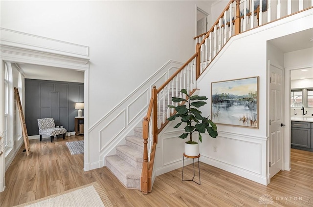 stairway with a high ceiling, a decorative wall, and wood finished floors