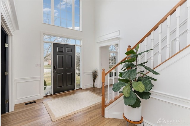 entryway with visible vents, stairway, wood finished floors, a high ceiling, and a decorative wall