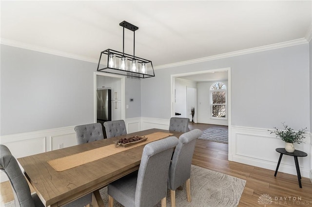 dining room with a wainscoted wall, crown molding, a decorative wall, and wood finished floors