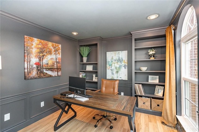 office space featuring light wood finished floors, built in features, a wainscoted wall, ornamental molding, and a decorative wall