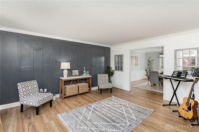 sitting room featuring ornamental molding, light wood-style floors, a chandelier, and a decorative wall