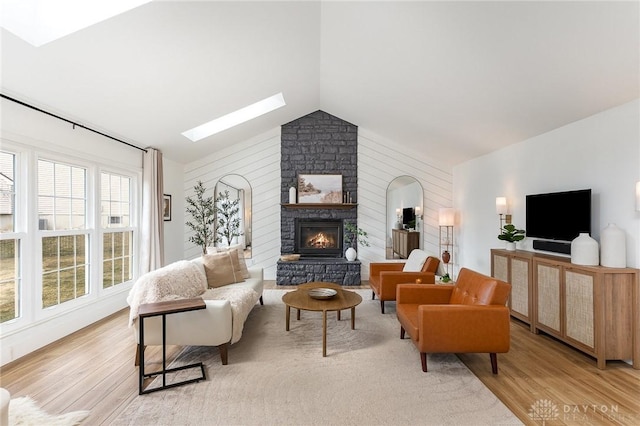 living area with light wood-style floors, a fireplace, and lofted ceiling with skylight