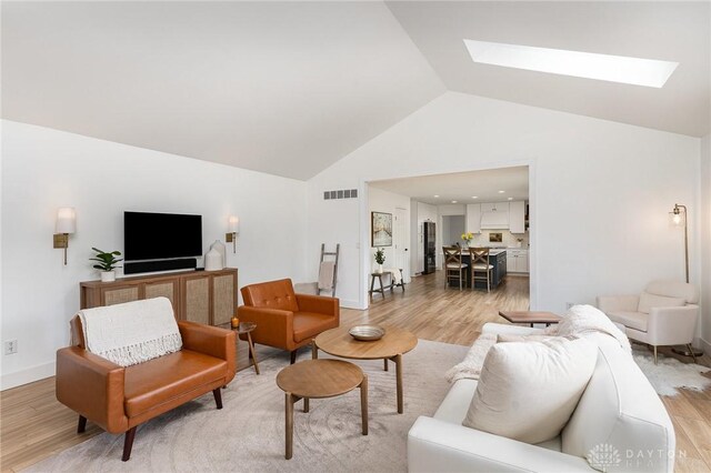 living area featuring a skylight, visible vents, light wood-style floors, high vaulted ceiling, and baseboards