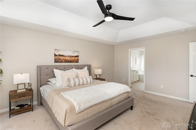 bedroom featuring a raised ceiling, light carpet, ensuite bath, and baseboards