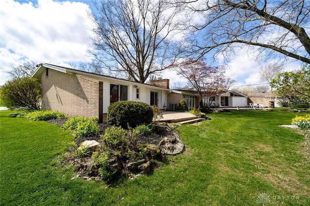 rear view of property with a deck, brick siding, a lawn, and a chimney