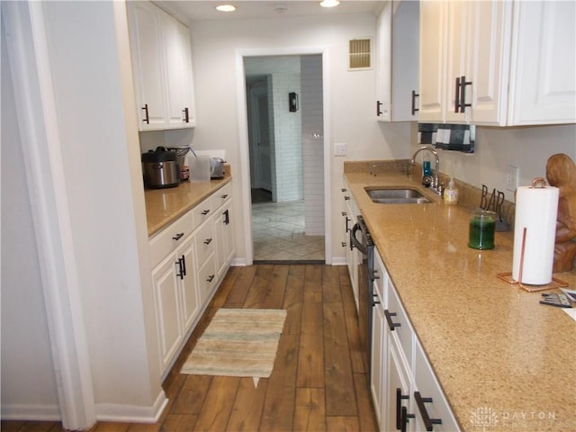 kitchen featuring dark wood-style floors, light stone counters, white cabinetry, a sink, and recessed lighting