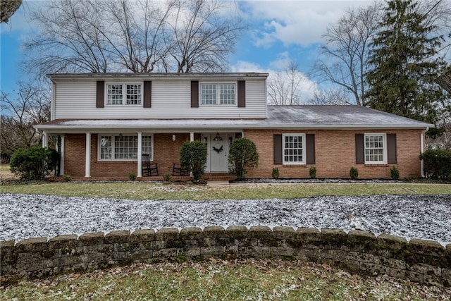 traditional-style house featuring a front yard, a porch, and brick siding