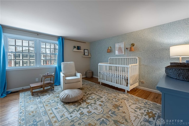 bedroom with a nursery area, wood finished floors, baseboards, and wallpapered walls