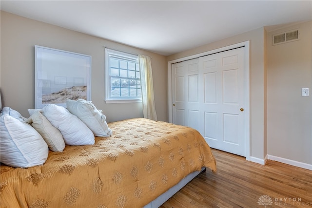 bedroom with a closet, visible vents, baseboards, and wood finished floors