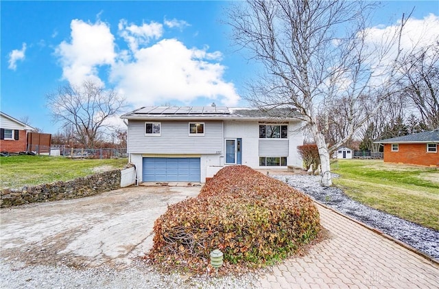 raised ranch with a garage, driveway, fence, and a front lawn