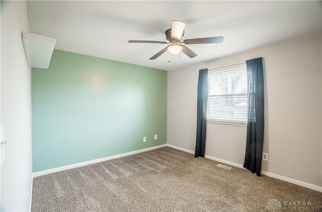 carpeted spare room featuring baseboards, visible vents, and ceiling fan