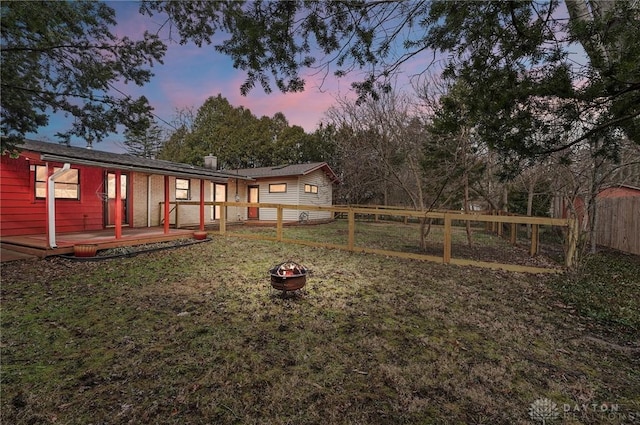 yard at dusk with fence, a fire pit, and a wooden deck