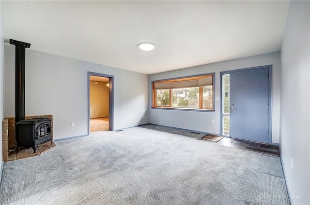 unfurnished living room with a wood stove, baseboards, and carpet flooring