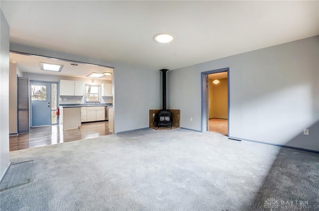 unfurnished living room with a wood stove, baseboards, and light colored carpet