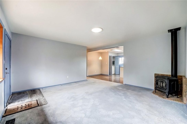 unfurnished living room featuring a wood stove, baseboards, and carpet floors