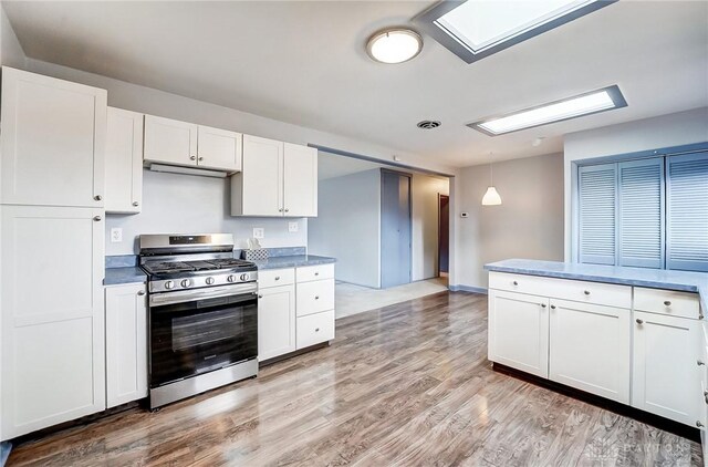 kitchen featuring stainless steel gas stove, light wood-style floors, white cabinetry, and decorative light fixtures