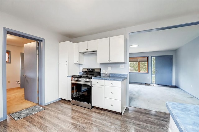 kitchen with dark countertops, light wood-style flooring, gas stove, white cabinetry, and baseboards