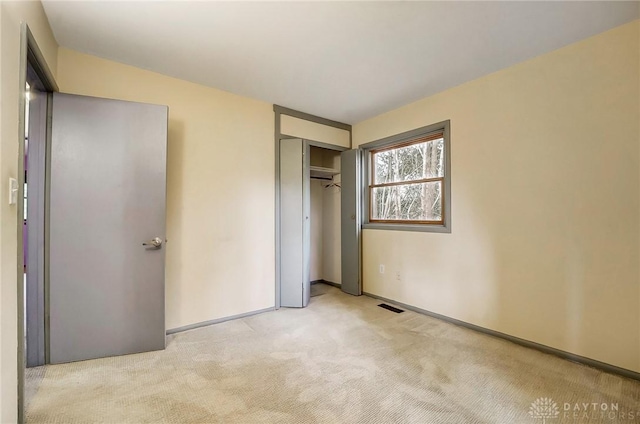 unfurnished bedroom with a closet, visible vents, light carpet, and baseboards