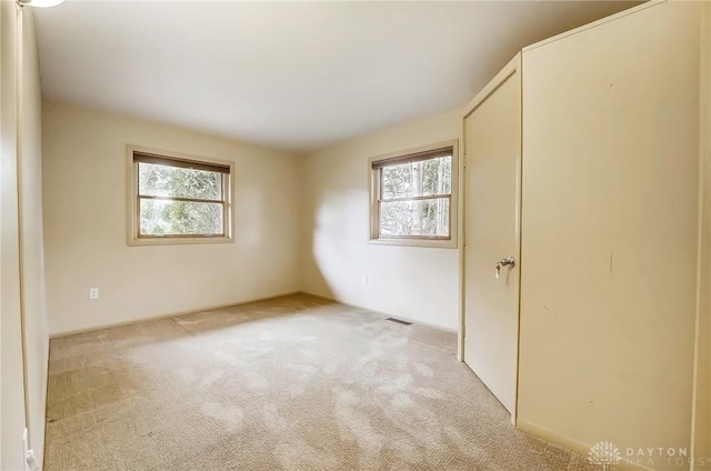 empty room featuring light carpet, visible vents, and a wealth of natural light