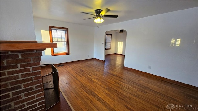 unfurnished living room with arched walkways, ceiling fan, dark wood-type flooring, visible vents, and baseboards