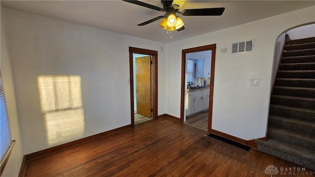 empty room with baseboards, visible vents, arched walkways, dark wood-style flooring, and stairs