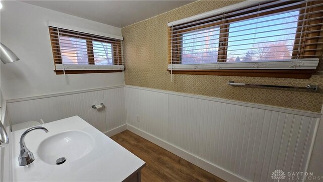 bathroom featuring a wainscoted wall, wood finished floors, a sink, and wallpapered walls