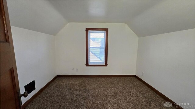 additional living space featuring lofted ceiling, dark carpet, and baseboards