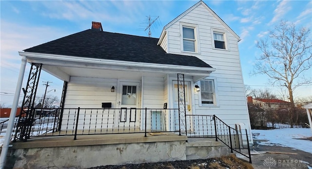 view of front of home featuring a porch, roof with shingles, and a chimney